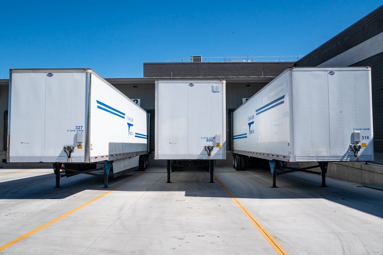 Sobre nosotros Three white cargo trailers parked at an industrial shipping dock under clear blue skies.